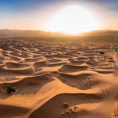 desert-landscape-with-sand-dunes-and-lone-road-aerial-view-of-arid-terrain-at-sunset